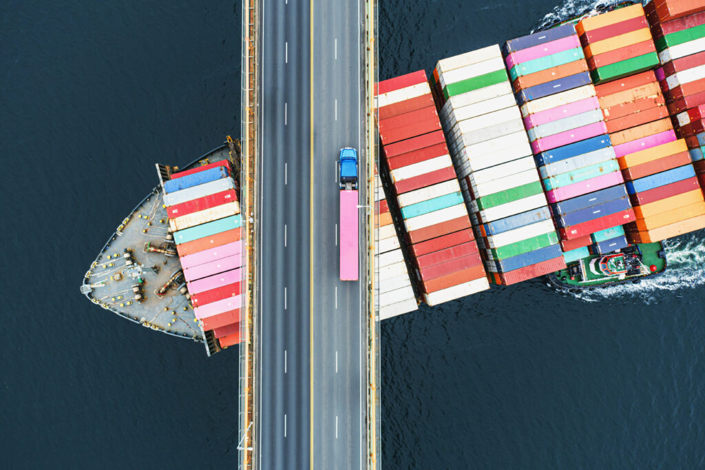 Aerial view of a container ship passing beneath a suspension bridge.