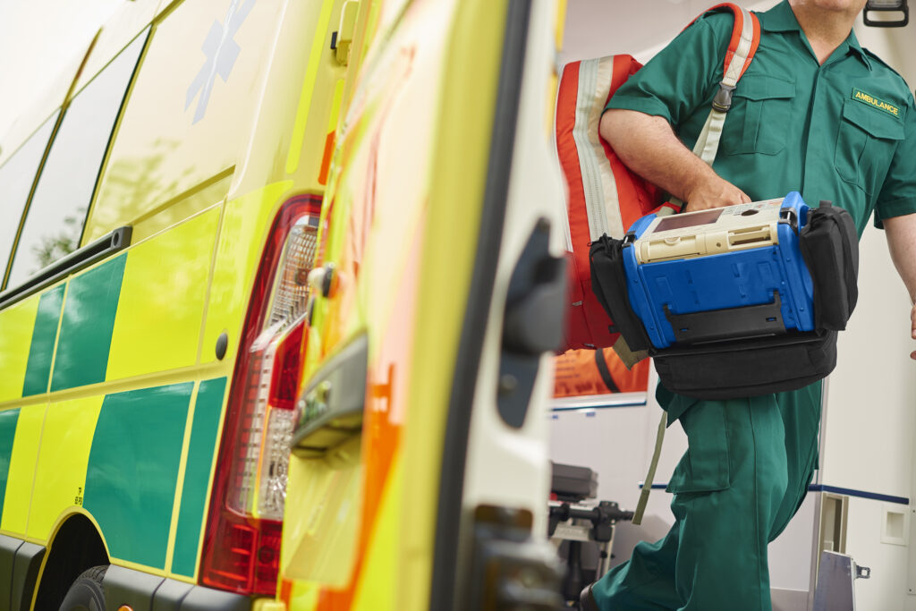 A first responder emerges from the back of an ambulance with his emergency backpack , and vital signs monitor.