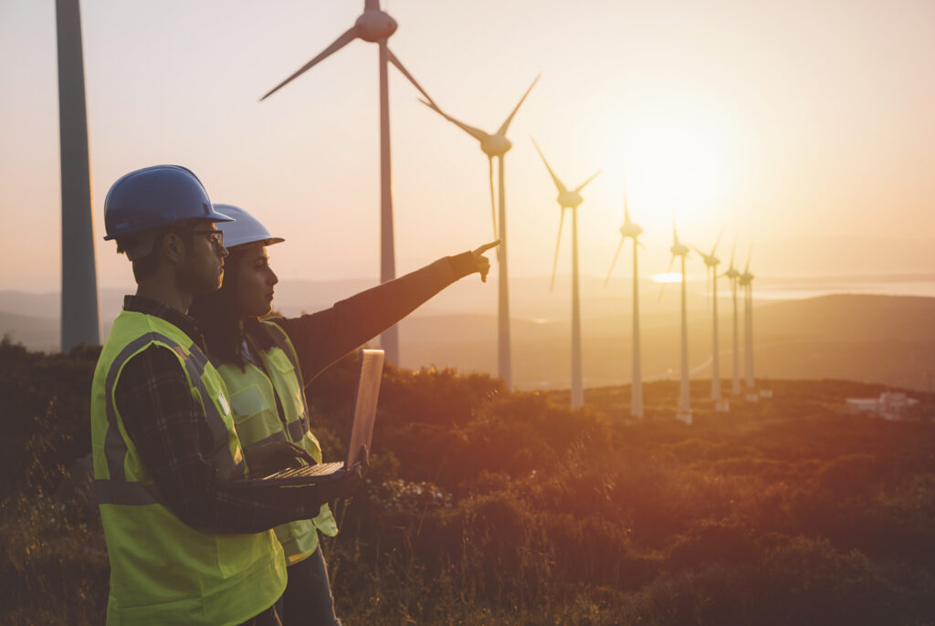 Maintenance engineer team working in wind turbine farm at sunset