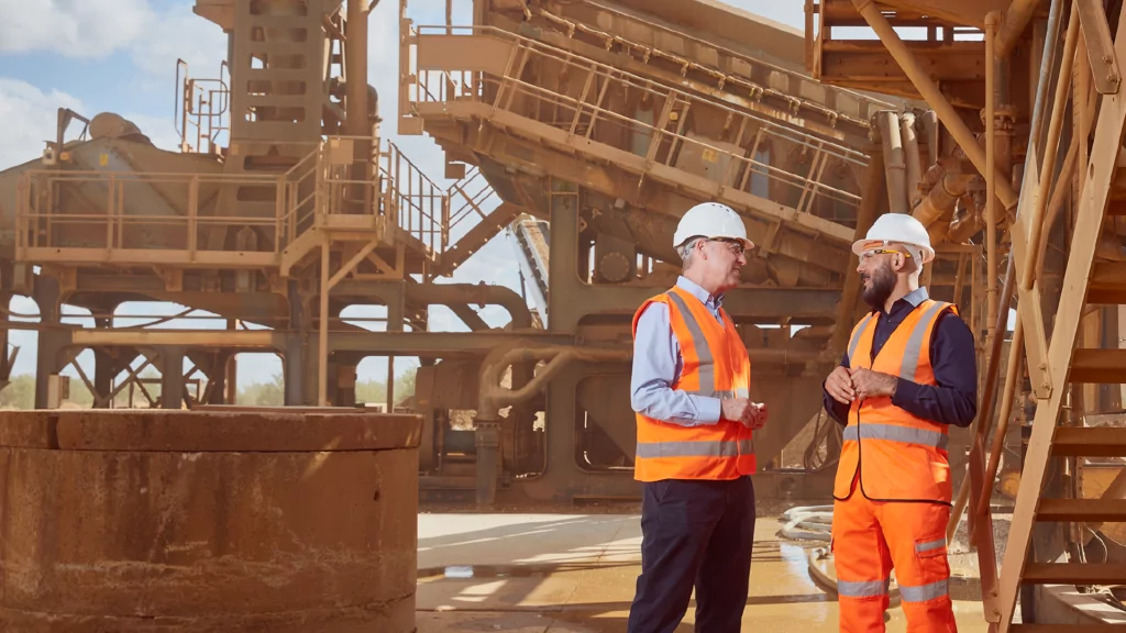 Two men wearing high visibility clothing speaking on a construction site.