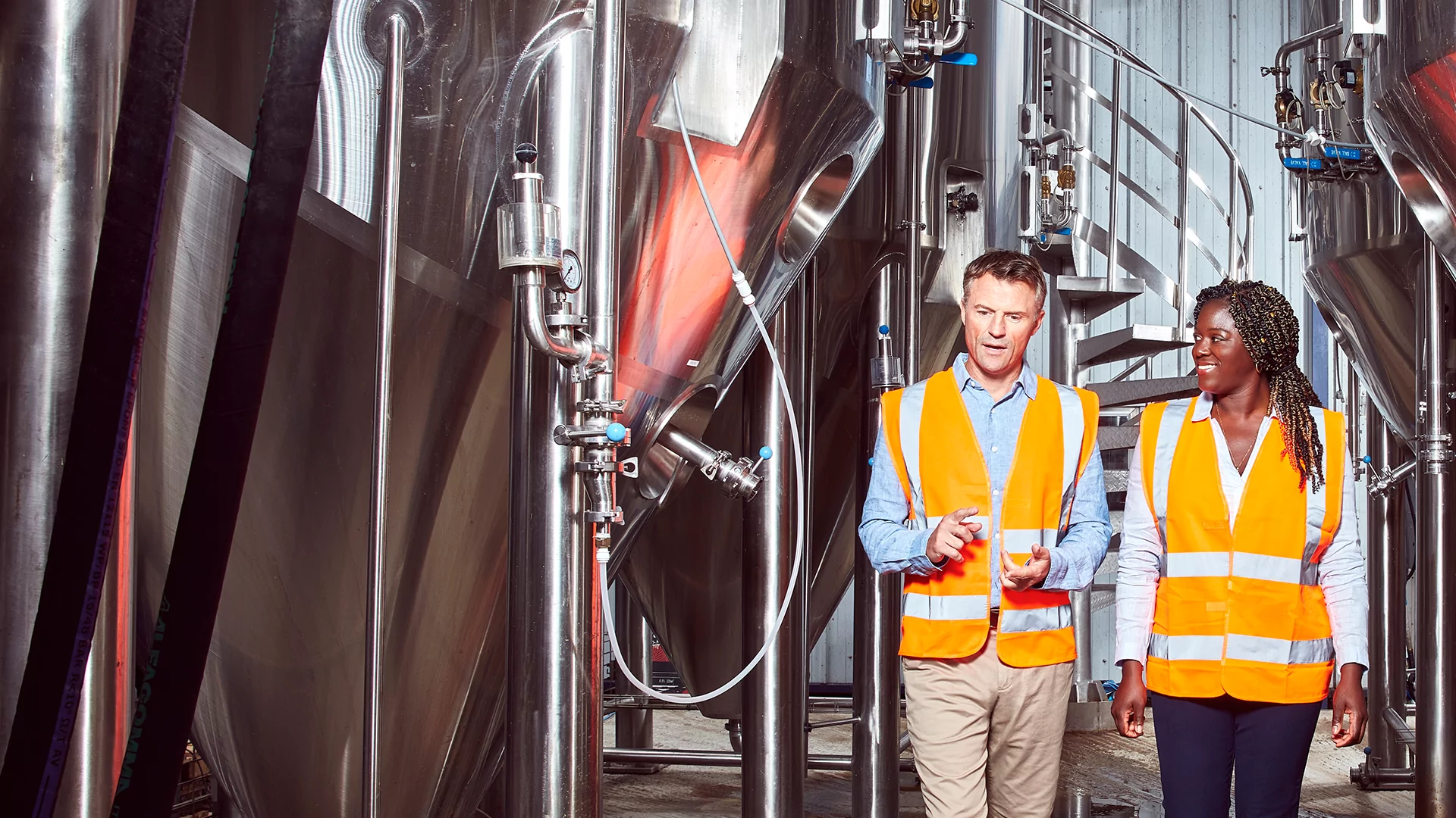 A man and a woman wearing high visibility vests chatting in a manufacturing facility.