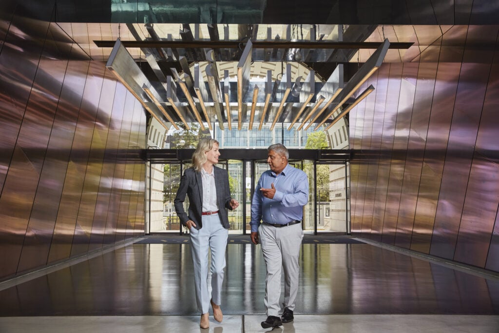 A man and woman talking while walking through an office building lobby.